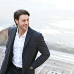 Confident man in a suit smiling while walking outdoors, showcasing fashion and style.